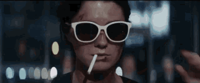 a woman wearing sunglasses and a cigarette in her mouth .