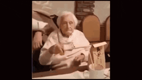 an older woman is sitting at a table with a cup of coffee .
