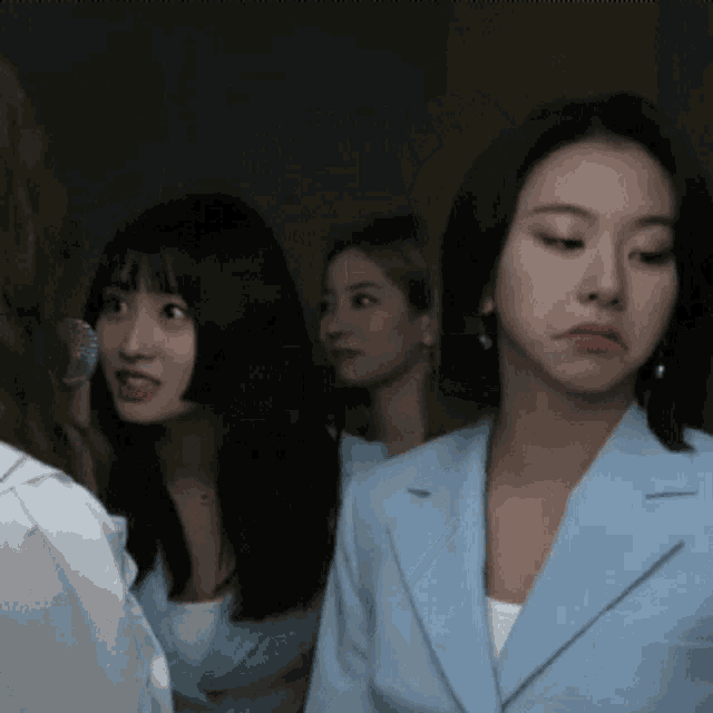 a group of women are standing in a dark room and one woman is wearing a blue jacket
