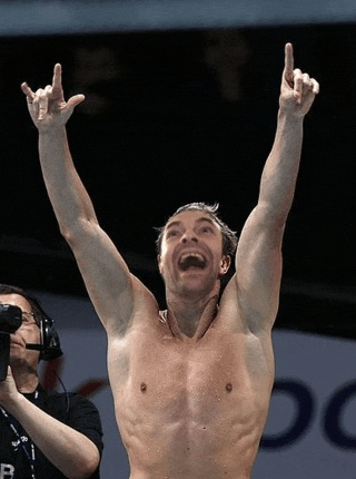 a shirtless man with his arms in the air and a cameraman behind him