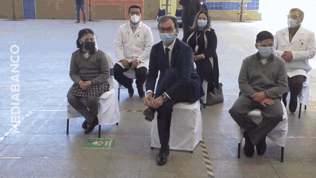 a group of people wearing face masks are sitting in front of a sign that says mediobanco