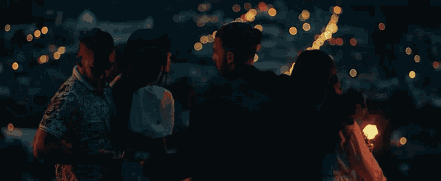 a group of people are standing in front of a city skyline at night