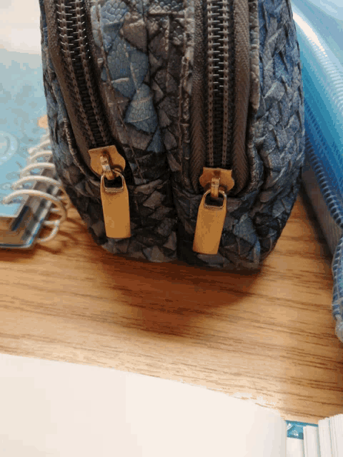 a blue purse with gold zipper pulls sits on a table