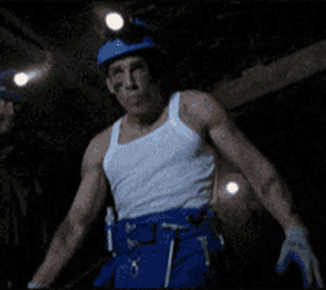 a man wearing a white tank top and blue pants is standing in the dark