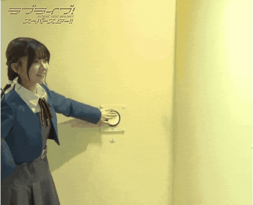 a girl in a blue jacket is pressing a button on a wall with school idol project written on it