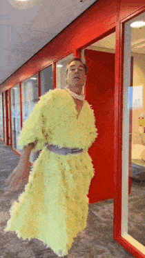 a man in a yellow dress is standing in a hallway with a red door