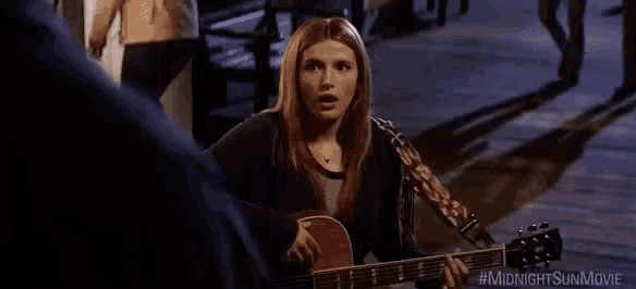 a woman is playing a guitar in a dark room while a man looks on .