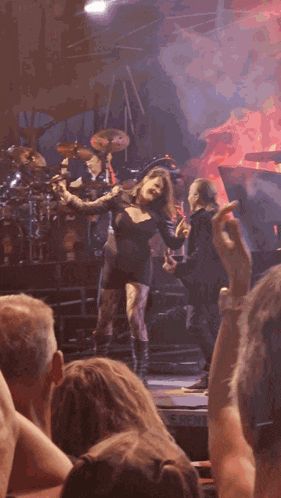 a woman in a black dress is dancing in front of a drum set