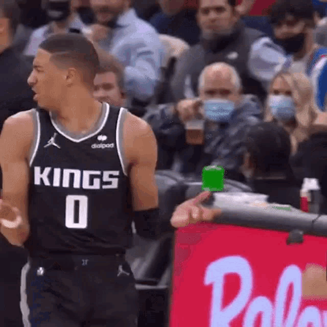 a basketball player in a kings jersey is standing in front of a crowd of people .
