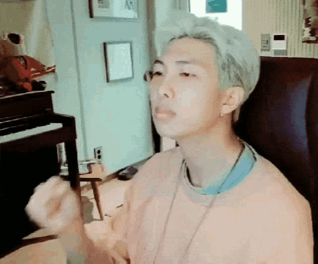 a man with white hair is sitting in a chair in front of a piano and making a funny face .