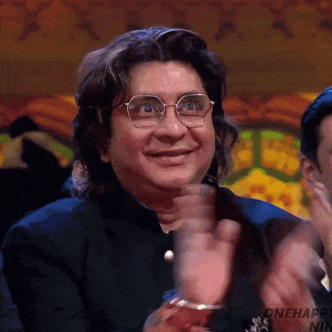 a man wearing glasses and a black suit is smiling and clapping his hands