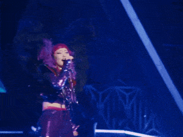 a woman singing into a microphone with purple hair