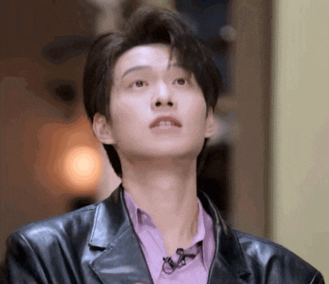 a young man wearing a leather jacket and a purple shirt is looking up at something .