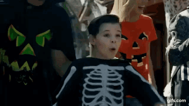 a boy in a skeleton costume is standing in a crowd of people .