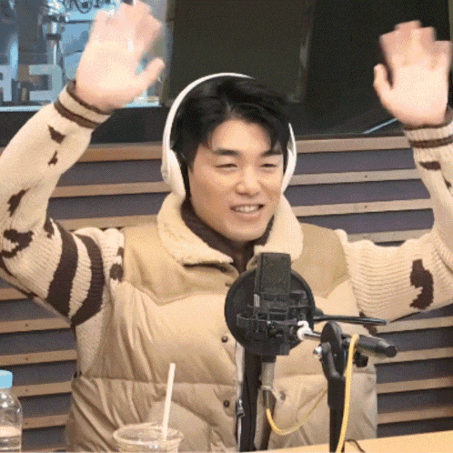 a man wearing headphones is sitting in front of a microphone with his hands in the air