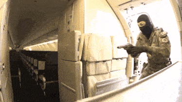 a man in a mask holds a gun in an airplane with a sign that says emergency exit