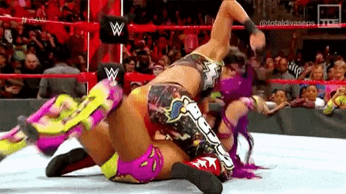 two female wrestlers are wrestling in a ring in front of a crowd .