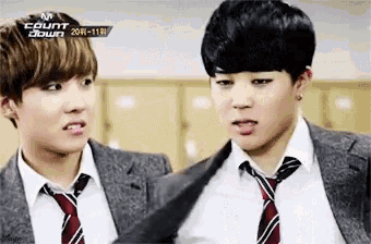 two young men in suits and ties are standing next to each other in a room .