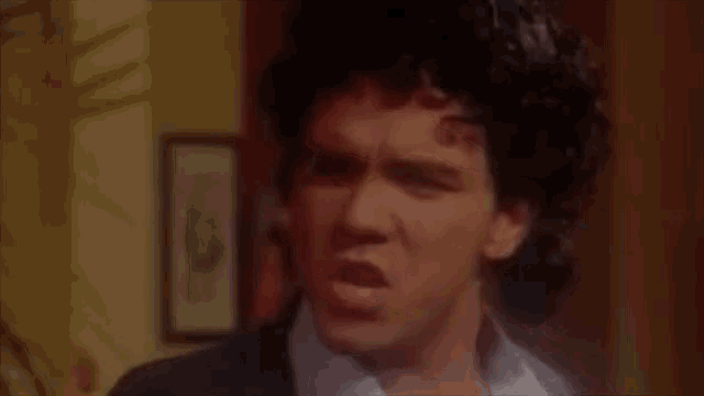 a man with curly hair is wearing a suit and a white shirt and looking at the camera .
