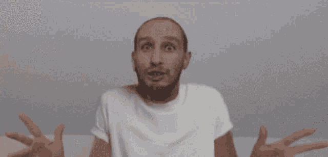 a bald man with a beard is wearing a white t-shirt and making a funny face