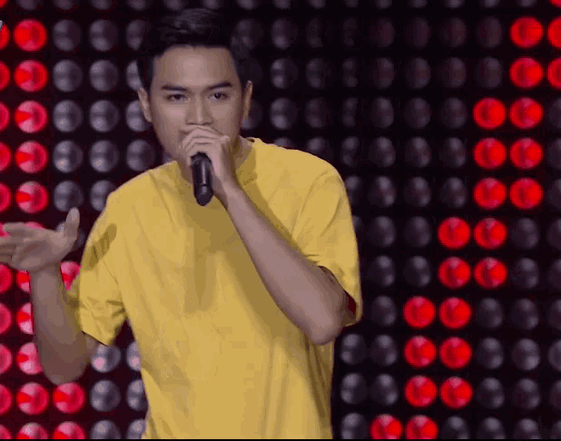 a man in a yellow shirt is singing into a microphone in front of a wall of lights