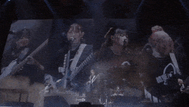 a group of girls playing guitars and drums on a stage with chinese writing on their shirts