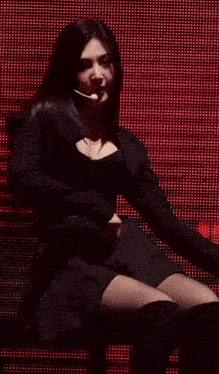 a woman in a black dress is sitting in front of a red screen .