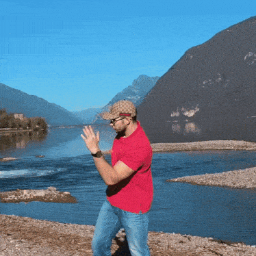 a man in a red shirt is standing in front of a body of water