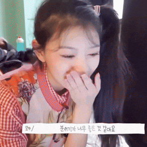 a girl with pigtails is covering her mouth with her hands in a room .