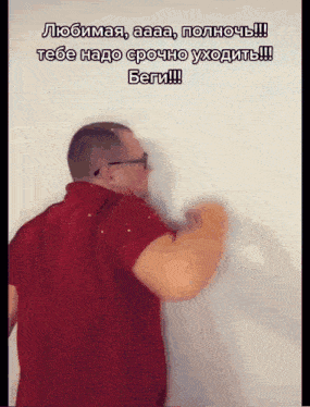 a man in a red shirt is standing in front of a white wall and says " любимая "