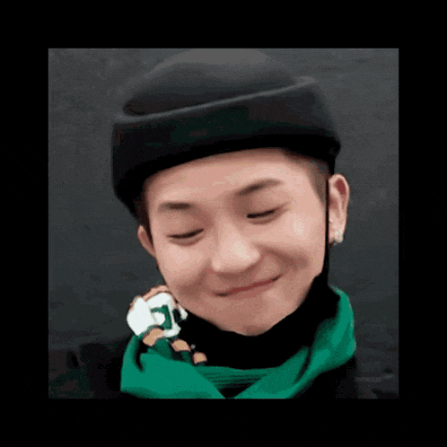 a young man wearing a black hat and a green scarf is smiling and holding a stuffed animal .