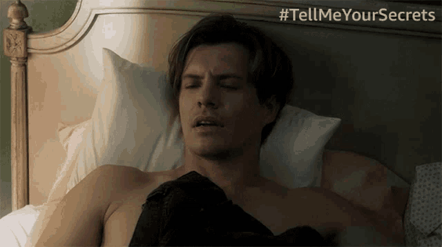 a shirtless man is laying on a bed with # tellmeyoursecrets written on the bottom right