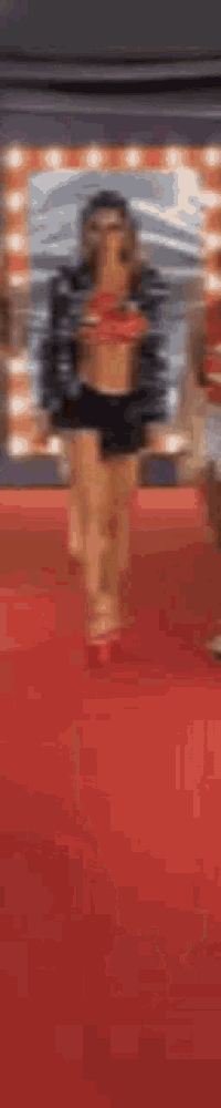 a woman is walking on a red carpet wearing shorts and a jacket .