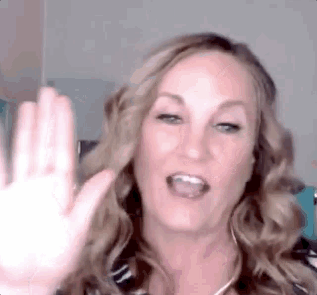 a woman is waving her hand in front of her face while talking on a video call .