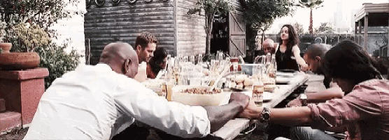 a group of people are sitting at a long table with their hands folded in prayer .