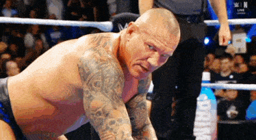 a wrestler with a lot of tattoos on his arms is kneeling down in a wrestling ring .
