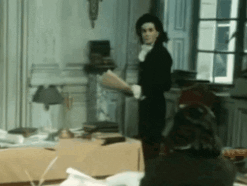 a man in a black suit is standing in a room holding a piece of paper
