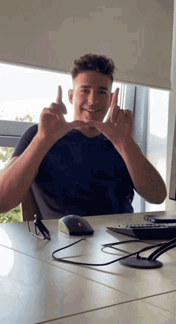 a man sitting at a desk with his hands in the shape of a heart