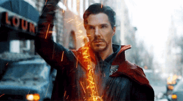 a man in a red cape is standing in front of a building holding a sword .