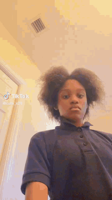 a young girl with curly hair is wearing a blue polo shirt and making a funny face .