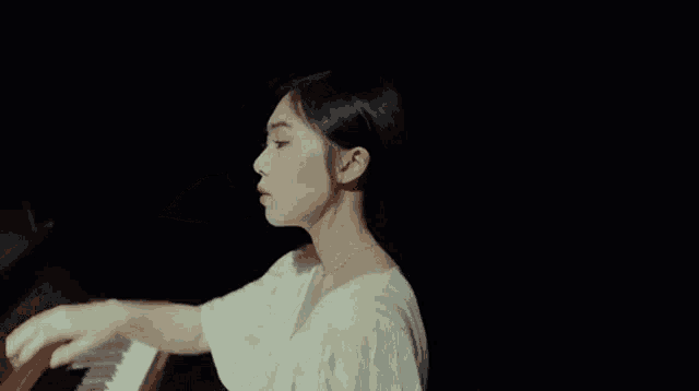 a woman in a white dress is standing in front of a piano and covering her face with her hand