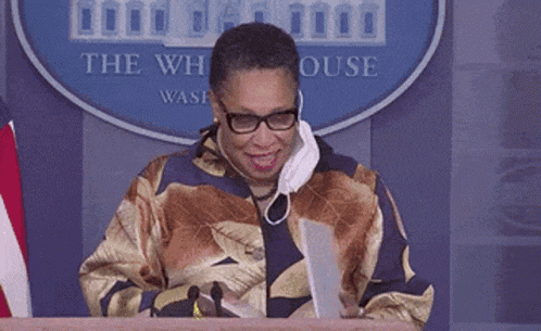 a woman wearing glasses and a mask is sitting at a podium in front of a white house logo .