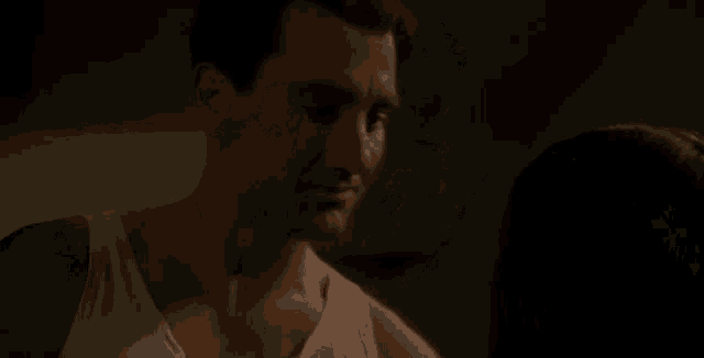 a man in a white tank top is talking to a woman in a dark room .