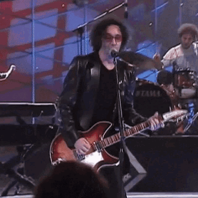 a man in a leather jacket is playing a guitar and singing into a microphone .