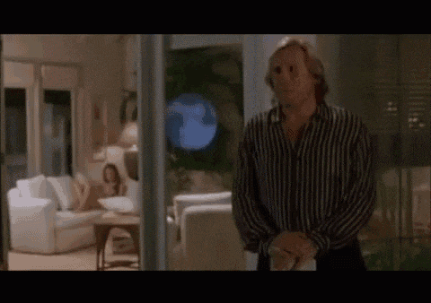 a man in a striped shirt is standing in a living room with a woman sitting on a couch in the background