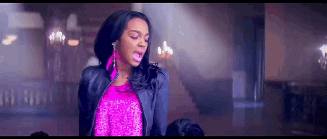 a woman in a pink top and purple jacket is singing into a microphone