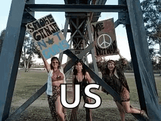 three women are standing next to each other holding signs in front of a metal structure .