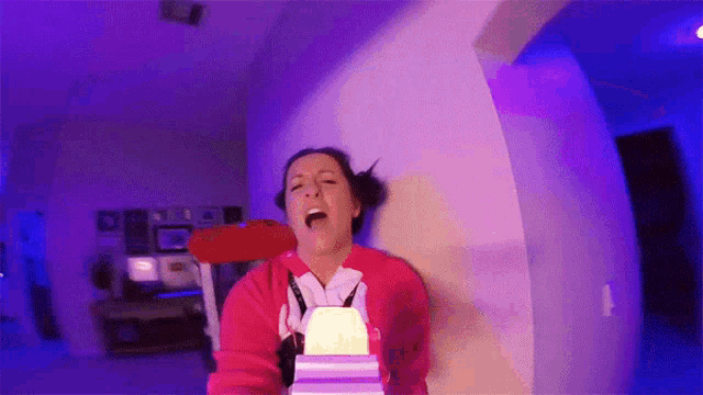 a woman in a red sweatshirt is screaming while holding a box in her hand .