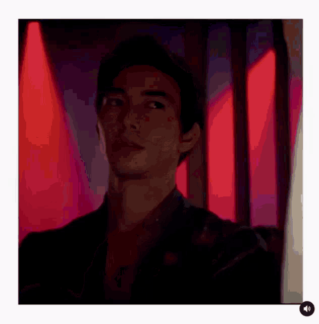 a man is standing in a dark room with red lights behind him and looking at the camera .