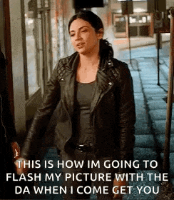 a woman in a leather jacket is standing on a sidewalk and talking to a man .